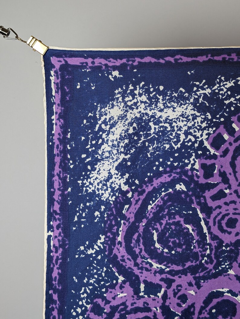 May include: A purple and blue patterned silk scarf with a white border. The scarf has a swirling design with a white background.