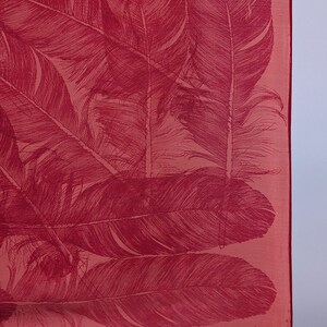 May include: A pink silk scarf with a red feather print. The scarf has a fringed edge and a small tag with the text "V.S.A.A."