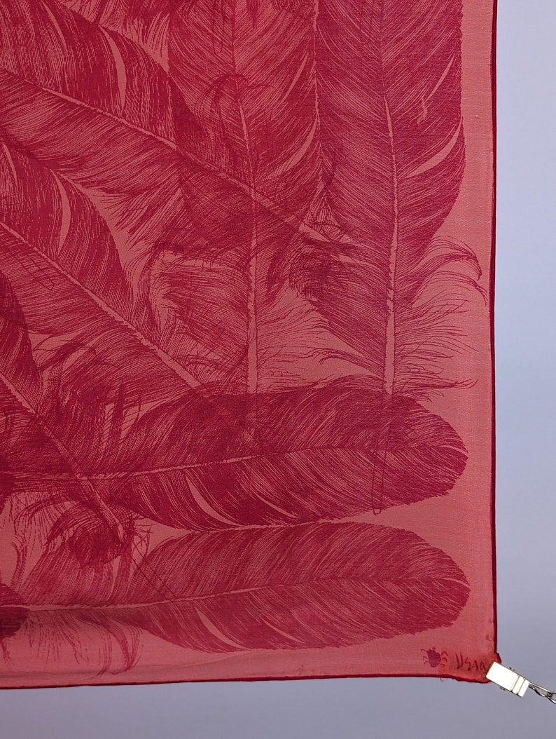 May include: A pink silk scarf with a red feather print. The scarf has a fringed edge and a small tag with the text "V.S.A.A."