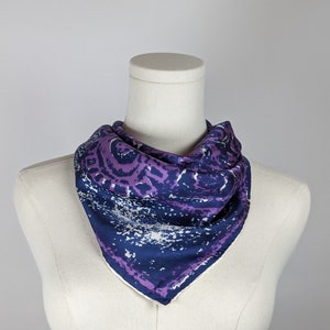 May include: A purple and blue patterned silk scarf with a white background. The scarf is folded into a triangle shape and is displayed on a white mannequin.