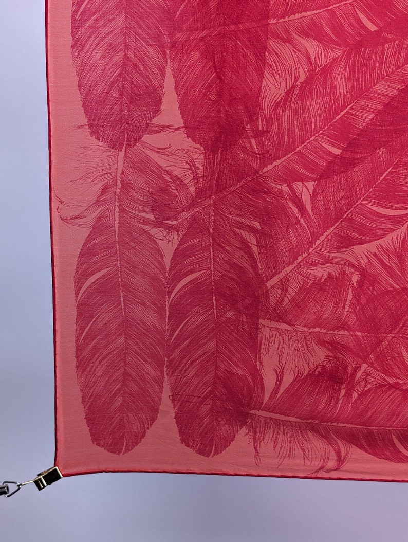 May include: A pink fabric scarf with a red feather pattern.