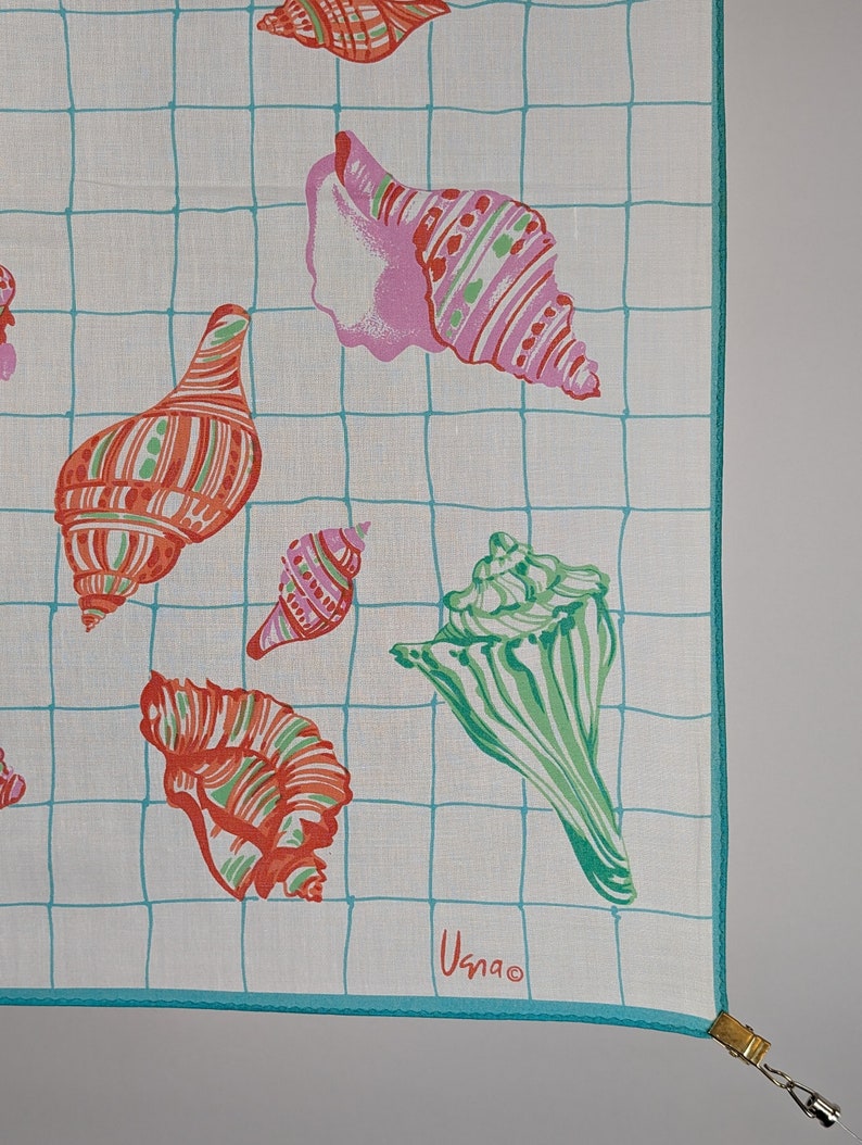 Op de afbeelding: Een wit katoenen zakdoek met een blauw rasterpatroon en kleurrijke schelpillustraties. Het zakdoek heeft een turquoise rand en de tekst "Usnao" is gedrukt in de rechterbenedenhoek.