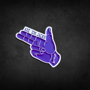 以下が含まれることがあります： 「AXE 'EM JACKS」と「SFA」の文字が白で書かれた紫色の手のジェスチャーピン。ピンには白い縁取りがあり、暗い背景に配置されています。ピンは学校の精神の象徴です。