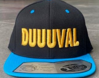 May include: Black and blue baseball cap with the word "DUUUVAL" embroidered in gold. The cap has a flat brim and a snapback closure. The cap has a blue brim and blue accents on the top.