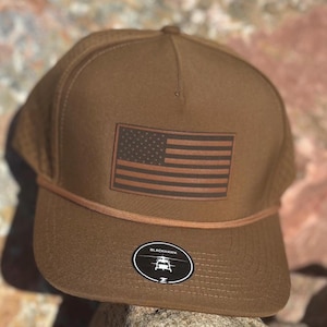 May include: A brown baseball cap with a brown leather American flag patch and a black and white logo that says "Blackhawk" on the front.