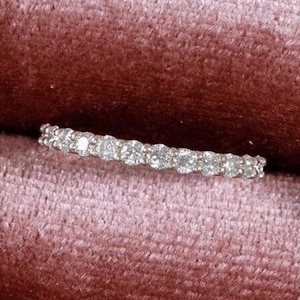 Pode incluir: Uma delicada aliança de eternidade de diamantes engastada em uma moldura de metal branco. O anel apresenta uma fileira de pequenos diamantes redondos que estão engastados bem juntos.