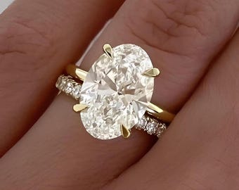 Pode incluir: Um anel de noivado de ouro com um grande diamante oval e uma banda de diamantes menor.