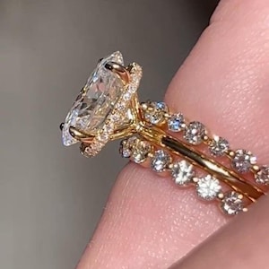 May include: A gold engagement ring with a large, clear, pear-shaped central stone. The ring has a halo of smaller diamonds around the central stone and along the band. A matching band with small diamonds is also visible.