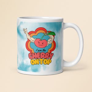 Könnte beinhalten: Eine weiße Keramiktasse mit blau-weißem Tie-Dye-Hintergrund. Eine Cartoon-Kirsche mit Gesicht und Armen hält einen Stiel. Der Text "I am the CHERRY ON TOP" ist auf die Tasse gedruckt.