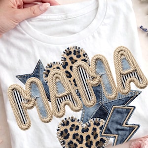 Może przedstawiać: Biała koszulka z napisem "MAMA". Litery obrysowane są sznurem i mają dżins i paski. Projekt zawiera dżinsowe gwiazdy, serca w panterkę i dżinsową błyskawicę.