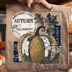 May include: A brown decorative pillow with an autumn theme. The pillow features a stitched pumpkin design with a distressed look, surrounded by leaves and the words "Autumn Fall Harvest". The pillow has a decorative stitched border.