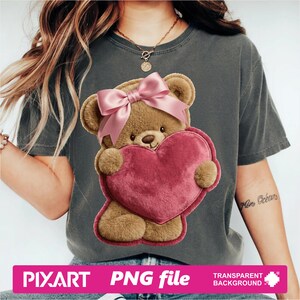 May include: Gray t-shirt featuring a brown teddy bear holding a pink heart. The teddy bear has a pink bow on its head. The image includes the text "PIXART PNG file TRANSPARENT BACKGROUND".