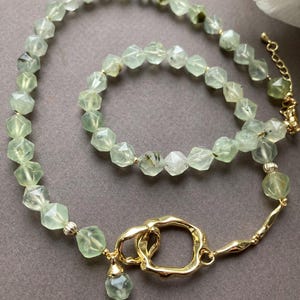 Op de afbeelding: Een groene edelsteen ketting en armband set met een gouden sluiting en een gouden hanger. De ketting heeft een unieke gouden sluiting met een cirkelvormig ontwerp.