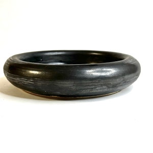 May include: A black ceramic bowl with a wide, rounded rim and a smooth, glossy finish. The bowl has a subtle, textured surface that gives it a unique look.