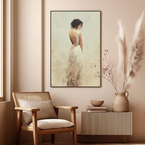 May include: A framed art print depicts a woman in a flowing white dress, her back to the viewer. The artwork has a soft, painterly style with neutral tones. The room features a wooden chair, a side table, and a vase with tall, feathery plants.