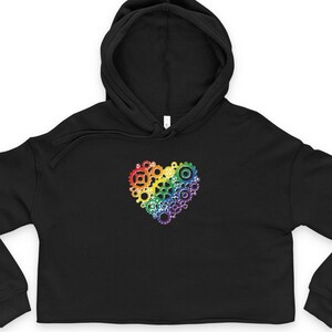 May include: Black cropped hoodie featuring a rainbow heart made of gears. The heart is centrally placed. The hoodie has a drawstring hood and long sleeves.