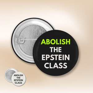 Może przedstawiać: Czarny guzik z napisem "ABOLISH THE EPSTEIN CLASS" w kolorze białym i zielonym. Guzik jest okrągły i ma metalowe plecy. Widoczny jest również mniejszy guzik z tym samym tekstem.