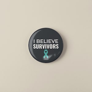 Könnte beinhalten: Ein runder, dunkelgrauer Button mit dem weißen Text "I BELIEVE SURVIVORS". Unter dem Text befindet sich eine türkisfarbene Schleife. Der Button befindet sich auf einem hellbeigen Hintergrund.