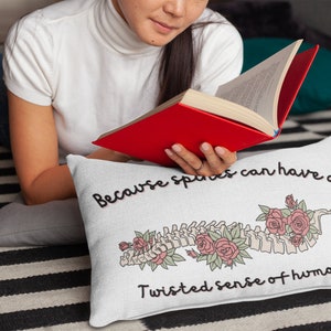May include: White throw pillow with a black and white illustration of a spine with roses and the text "Because spines can have a twisted sense of humor."