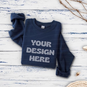 Puede incluir: Una sudadera azul marino de manga larga con cuello redondo que presenta el texto "YOUR DESIGN HERE" en una fuente sans-serif redondeada de color gris claro centrada en el pecho. La prenda tiene cuello, puños y dobladillo acanalados y una etiqueta.