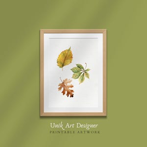 Puede incluir: Una pintura de acuarela enmarcada de tres hojas de otoño. Las hojas son amarillas, verdes y marrones. La pintura está sobre un fondo blanco y tiene un marco de madera.