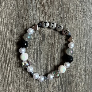 May include: A white and black beaded bracelet with silver letter beads spelling "TTPD" and silver heart charms.