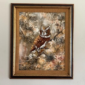 May include: A framed painting of an owl perched on a branch in a forest setting. The owl is brown and white with a yellow beak and large, dark eyes. The background is a mix of brown, green, and white.