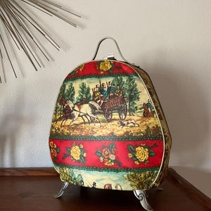May include: A vintage, egg-shaped, hard-sided suitcase with a floral and horse-drawn carriage print. The suitcase has a silver handle and three silver feet.