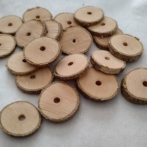 May include: A pile of natural wood round slices with a hole in the center. The wood is a light brown color and the edges are rough. The slices are about 1 inch in diameter.
