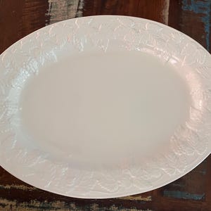 May include: An oval, off-white serving platter with a raised leaf design around the rim. The platter is made of ceramic or porcelain and is suitable for serving food at a dinner party or holiday gathering.