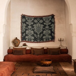 Peut inclure: Intérieur de salon avec une tapisserie florale sombre à franges, au-dessus d'un canapé rouille avec des coussins bruns. Un bol en bois et un tapis à motifs complètent la décoration.