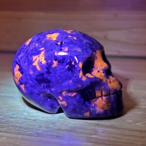May include: A purple and orange skull made of polished stone. The skull is carved in detail and has a smooth, glossy finish.