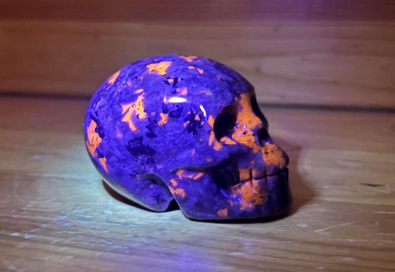 May include: A purple and orange skull made of polished stone. The skull is carved in detail and has a smooth, glossy finish.