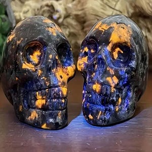 May include: Two black and blue skull-shaped crystal carvings with orange and yellow accents.