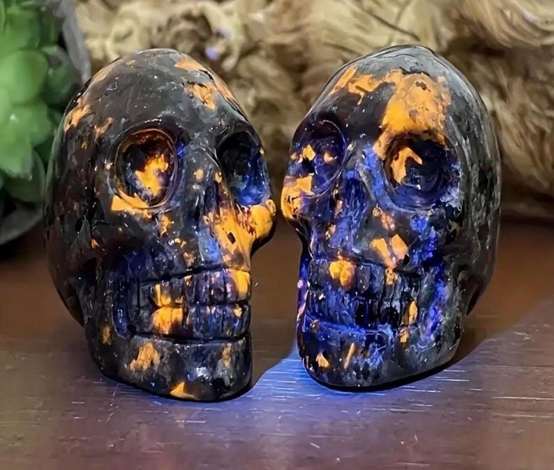 May include: Two black and blue skull-shaped crystal carvings with orange and yellow accents.