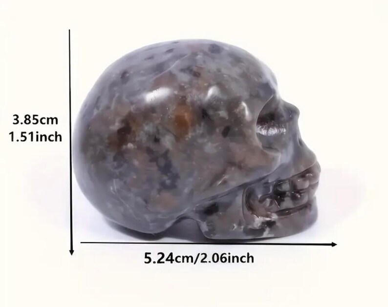 May include: A dark gray and brown skull sculpture made of polished stone. The skull is approximately 1.51 inches tall and 2.06 inches wide.