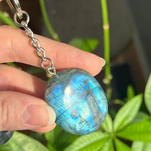Può includere: Un portachiavi in labradorite blu con una catena d'argento. La pietra ha un bagliore iridescente.