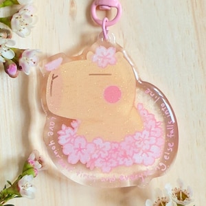 May include: A pink and white capybara charm with a pink flower garland and the text "Love you more than words can say, 'cause even the stars fall into place when I'm with you."