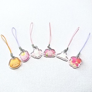 May include: A collection of six clear acrylic charms with various cartoon designs, including a cat, a bunny, and a cloud. Each charm has a different color lanyard attached, such as orange, pink, and purple. The charms are small and detailed.
