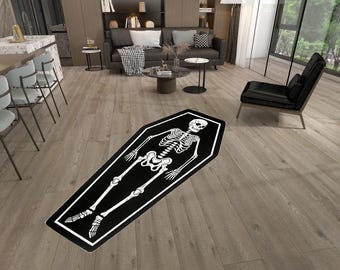May include: A rectangular area rug shaped like a coffin featuring a white skeleton graphic printed on a black background. The rug has a thick white border outlining the coffin shape, with the skeleton positioned centrally within the black interior space.