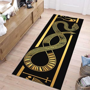 May include: A rectangular runner rug featuring a black background with a large, stylised golden snake coiled in an infinity-like pattern. The design includes golden border lines and additional geometric symbols at the top and bottom edges.