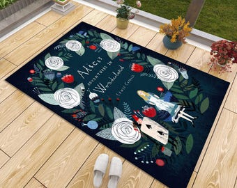 May include: A rectangular floor mat with a dark blue background featuring a floral wreath design, white roses, and illustrations of Alice and a playing card character. The text reads Alice's Adventures in Wonderland by Lewis Carroll.