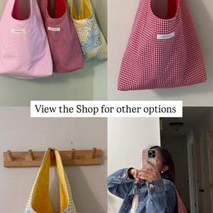 Op de afbeelding: Een verzameling tote tassen in verschillende patronen en kleuren, hangend aan houten pinnen. De tassen omvatten roze gingham, rode gingham en een patchwork ontwerp met gele en blauwe bloempatronen. De tekst "View the Shop for other options" is zichtbaar.