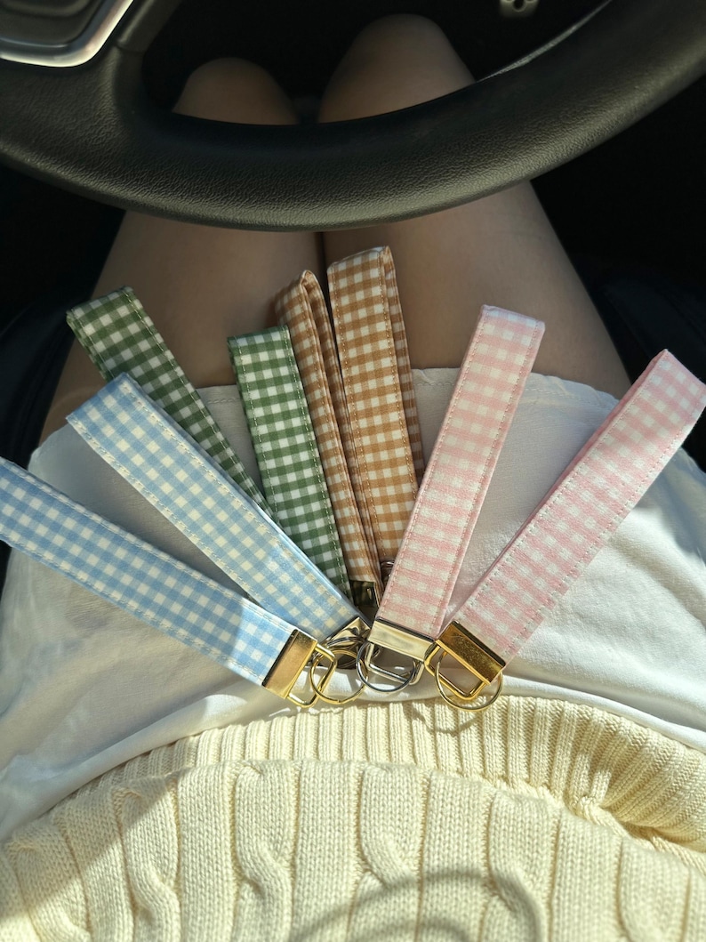 May include: A collection of keychains in various colors, including light blue, green, tan, and pink. Each keychain features a gingham pattern and a gold-colored metal clasp.