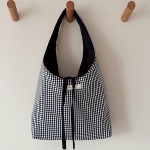 May include: Black and white gingham tote bag with black fabric lining and a black ribbon tie. The bag has a white label with the text "Little Wren" on it.