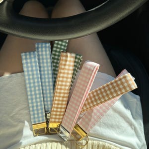 May include: Six different colored gingham keychains with gold key rings. The keychains are light blue, brown, pink, green, and two shades of pink.