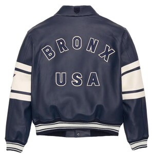 May include: A navy blue leather jacket with white accents and the word "BRONX USA" in white lettering on the back. The jacket has a classic varsity style with a ribbed hem and cuffs, and white stripes on the sleeves.