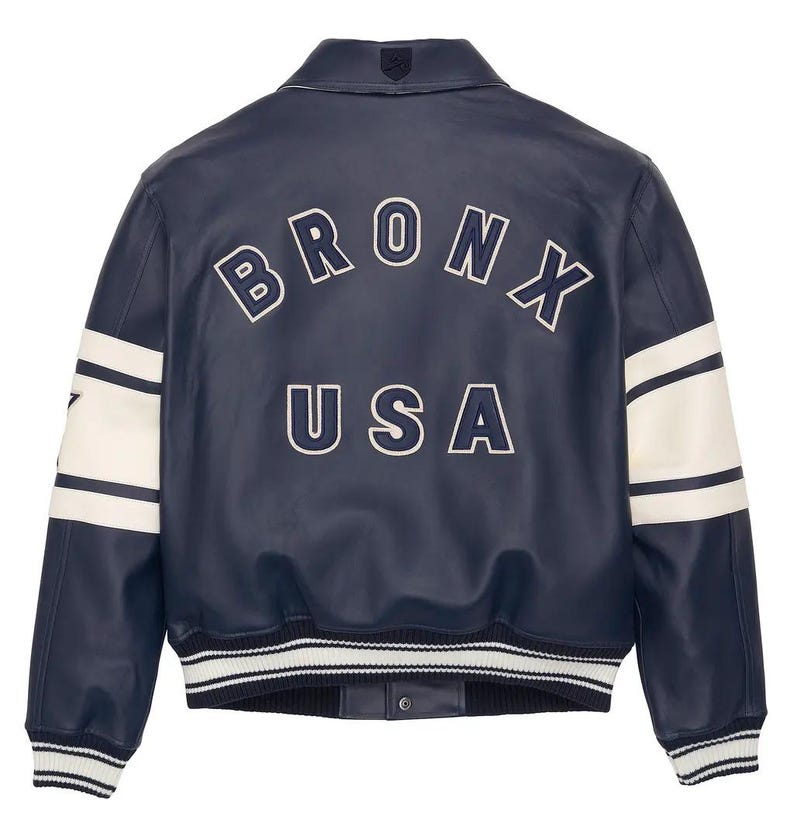 May include: A navy blue leather jacket with white accents and the word "BRONX USA" in white lettering on the back. The jacket has a classic varsity style with a ribbed hem and cuffs, and white stripes on the sleeves.