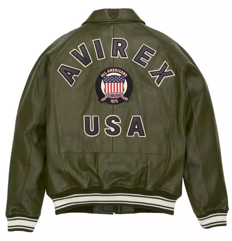 May include: Olive green leather jacket with the word "AVIREX" across the back in white lettering. A patch with the American flag and the words "ALL AMERICANS ESTABLISHED 1975" is centered below the lettering. The word "USA" is below the patch.