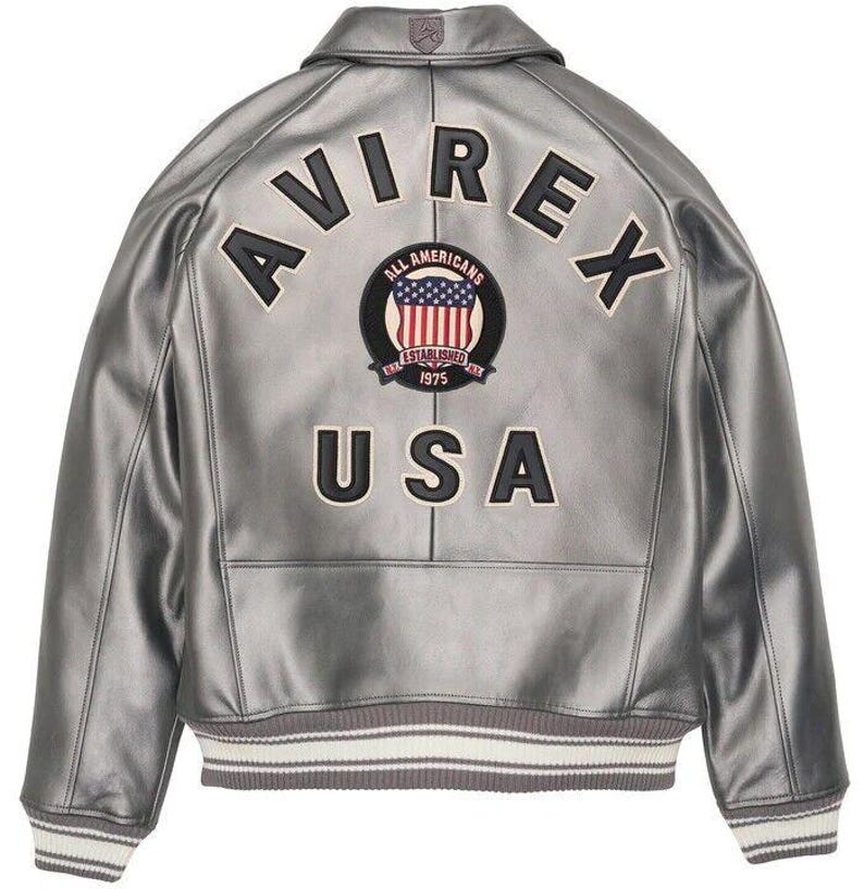 May include: Silver leather jacket with the word "AVIREX" across the back, above a circular patch with the American flag and the words "ALL AMERICANS ESTABLISHED 1975 USA". The jacket has a ribbed collar and cuffs.